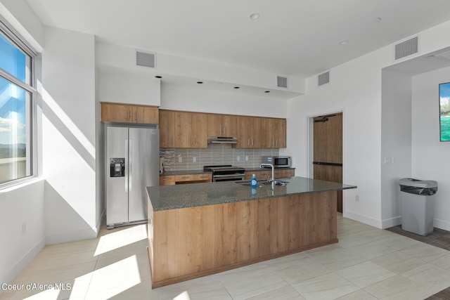 kitchen featuring appliances with stainless steel finishes, a kitchen island with sink, tasteful backsplash, and light tile floors