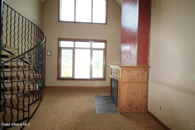 interior space with a towering ceiling, a tiled fireplace, and dark carpet