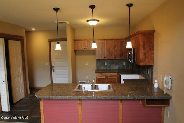 kitchen featuring dark tile floors, sink, backsplash, hanging light fixtures, and kitchen peninsula