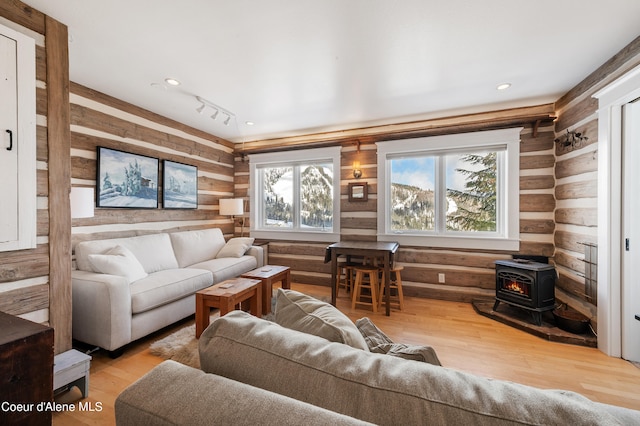 living room with log walls, a wood stove, rail lighting, and hardwood / wood-style flooring