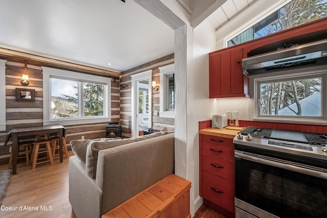 kitchen featuring fume extractor, light hardwood / wood-style flooring, stainless steel range with gas cooktop, rustic walls, and lofted ceiling