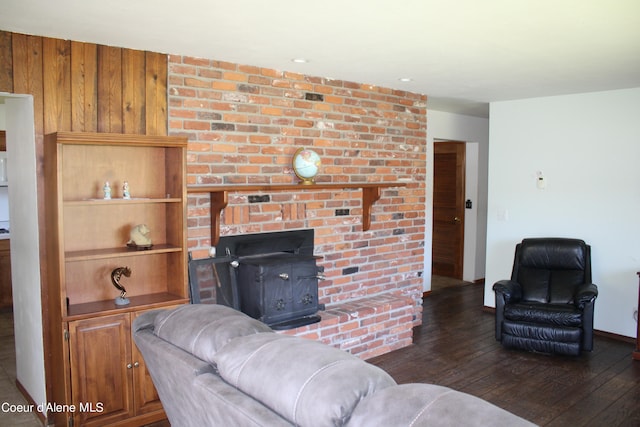 living room with wood walls, brick wall, dark wood-type flooring, a fireplace, and a wood stove