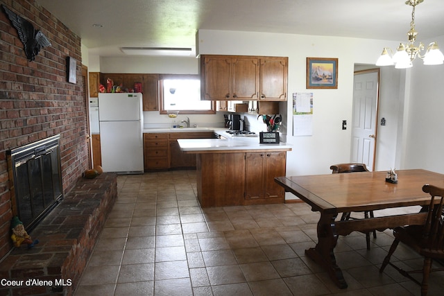 kitchen with pendant lighting, a fireplace, an inviting chandelier, white fridge, and dark tile flooring