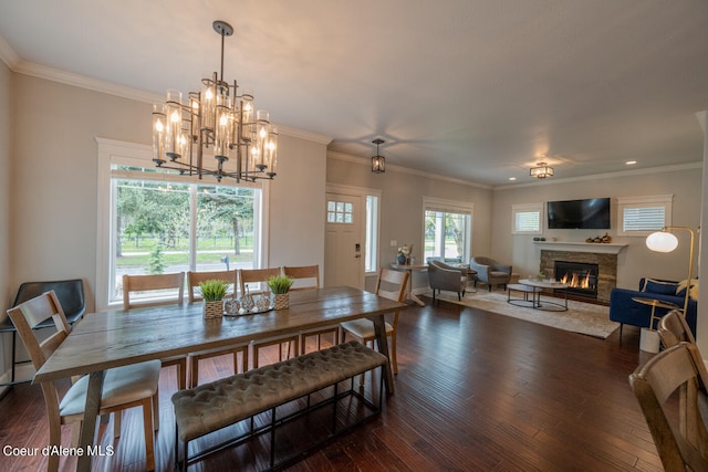 dining room with ornamental molding, a notable chandelier, a stone fireplace, and dark wood-type flooring