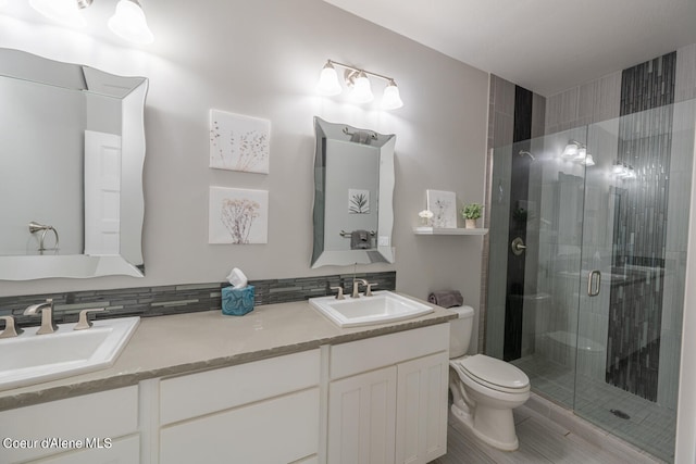 bathroom featuring a shower with door, dual vanity, tasteful backsplash, and toilet