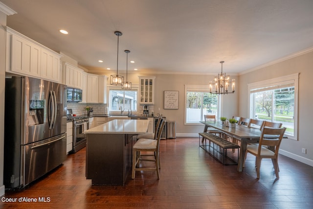 kitchen with appliances with stainless steel finishes, a kitchen island, tasteful backsplash, dark wood-type flooring, and decorative light fixtures