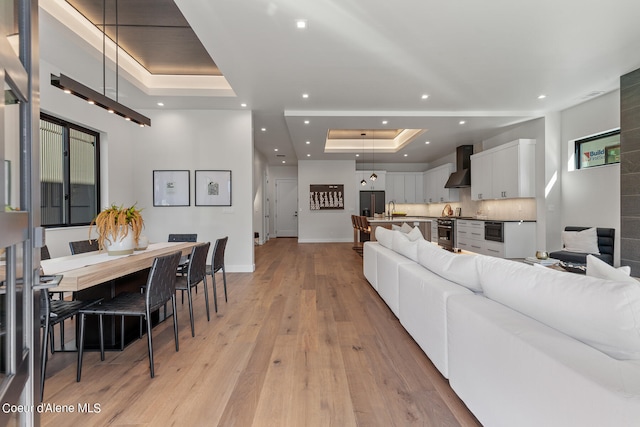 living room featuring a raised ceiling, sink, and light hardwood / wood-style flooring