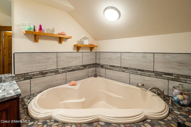 bathroom with vaulted ceiling, a bath to relax in, vanity, and a textured ceiling