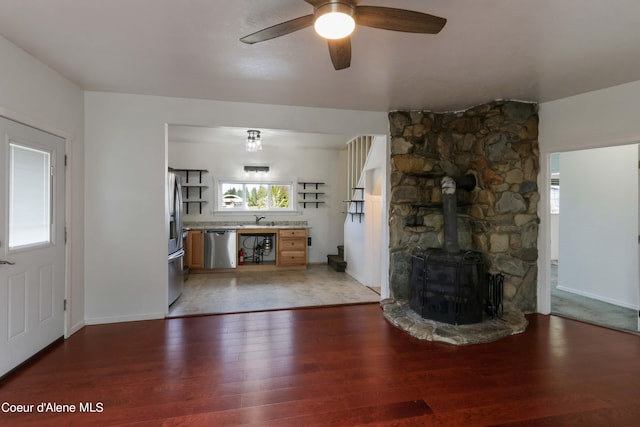 unfurnished living room featuring dark hardwood / wood-style flooring, a wood stove, ceiling fan, and sink