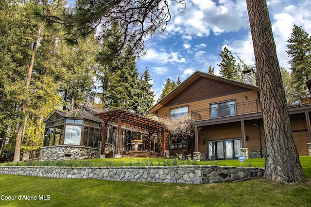 rear view of property with a pergola, a balcony, and a lawn