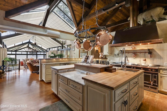 kitchen featuring light wood-type flooring, butcher block countertops, a kitchen island with sink, beam ceiling, and backsplash