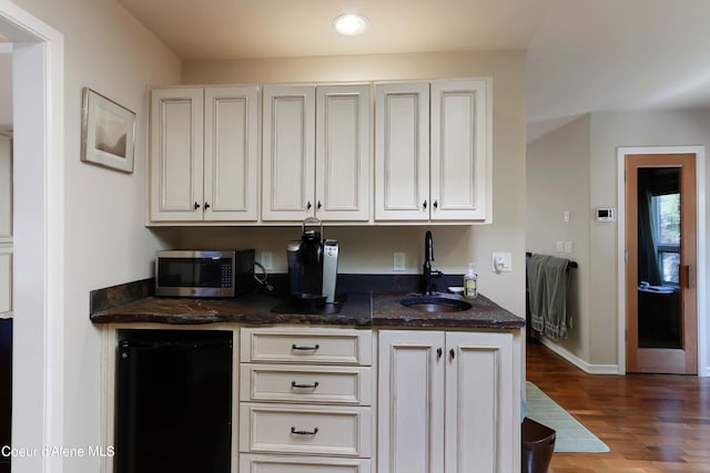 kitchen featuring dark stone countertops, white cabinets, hardwood / wood-style flooring, fridge, and sink