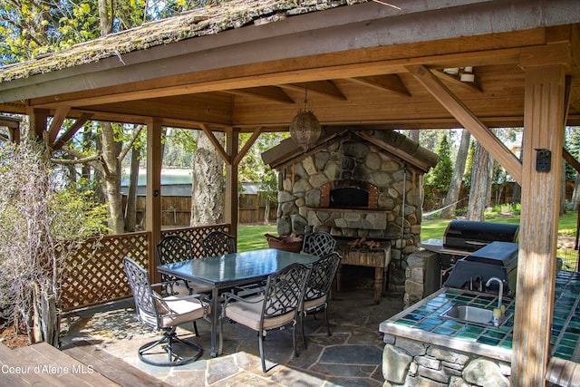 view of patio with sink, an outdoor stone fireplace, and a gazebo