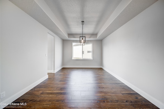 spare room with dark hardwood / wood-style floors, a tray ceiling, a textured ceiling, and a chandelier