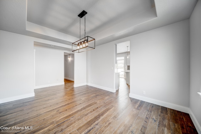 unfurnished dining area with a raised ceiling, an inviting chandelier, and hardwood / wood-style floors