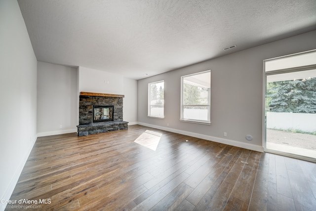 unfurnished living room featuring a stone fireplace, a textured ceiling, and wood-type flooring