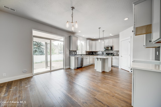 kitchen featuring decorative light fixtures, backsplash, stainless steel appliances, hardwood / wood-style floors, and a center island