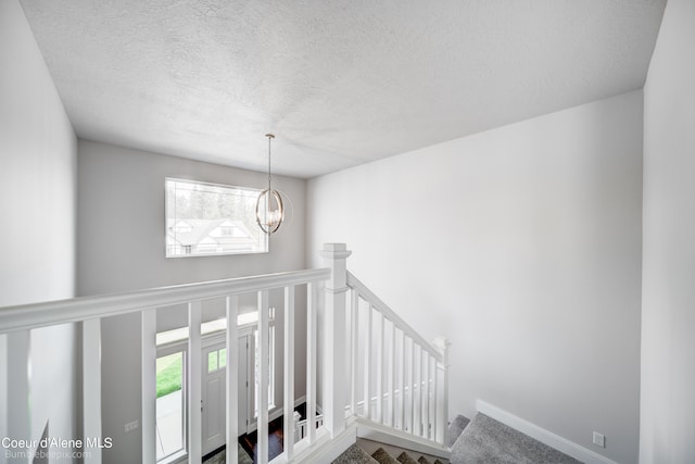 stairway featuring a chandelier, a textured ceiling, and carpet floors