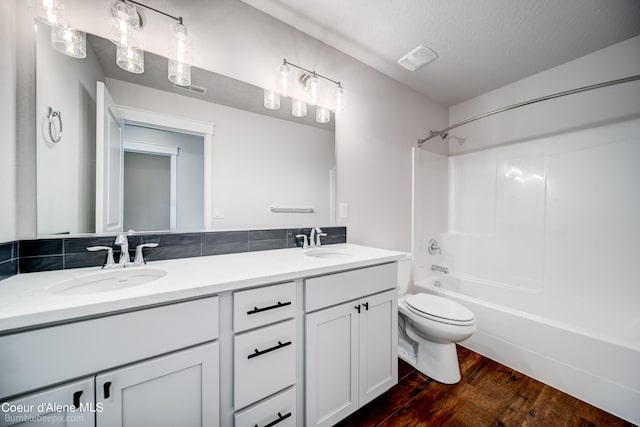 full bathroom with double sink vanity, shower / bathing tub combination, wood-type flooring, tasteful backsplash, and toilet