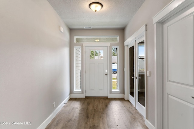 foyer entrance featuring french doors, a textured ceiling, and wood-type flooring