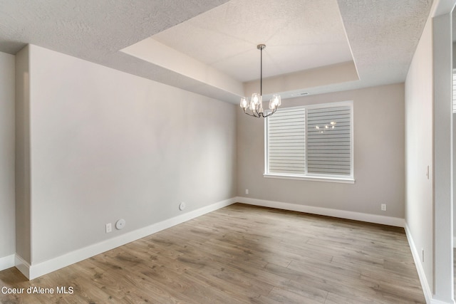 empty room with an inviting chandelier, a textured ceiling, light hardwood / wood-style floors, and a raised ceiling