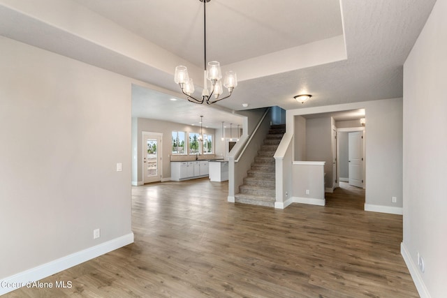 unfurnished room with wood-type flooring, an inviting chandelier, and a raised ceiling