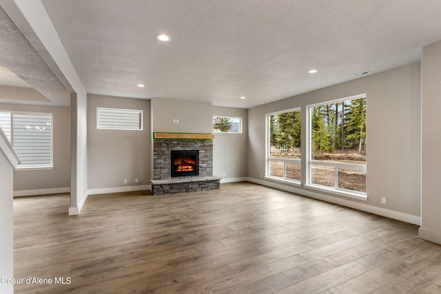 unfurnished living room with a stone fireplace, light hardwood / wood-style floors, and a textured ceiling