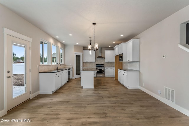 kitchen featuring hanging light fixtures, backsplash, wall chimney range hood, a center island, and appliances with stainless steel finishes