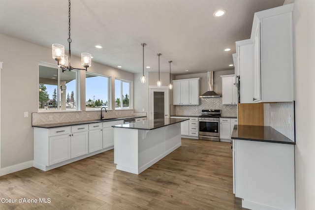 kitchen featuring a center island, wall chimney range hood, stainless steel stove, pendant lighting, and tasteful backsplash