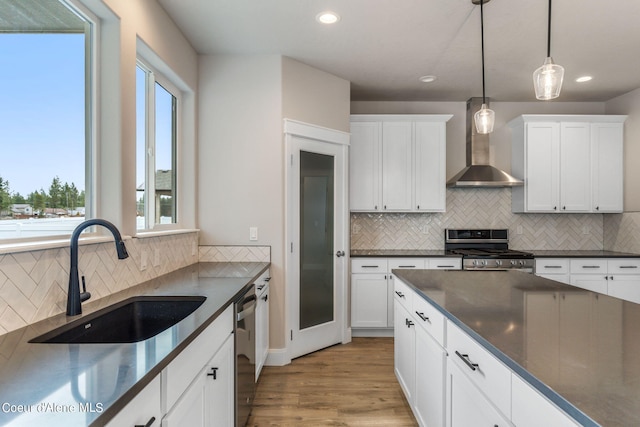 kitchen with wall chimney range hood, light hardwood / wood-style floors, appliances with stainless steel finishes, sink, and tasteful backsplash