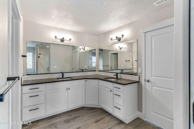 bathroom with a textured ceiling, wood-type flooring, and vanity with extensive cabinet space