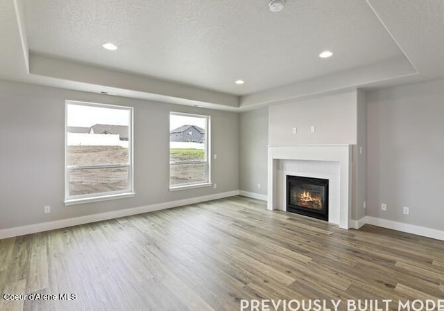 unfurnished living room featuring hardwood / wood-style floors, a tray ceiling, and a textured ceiling