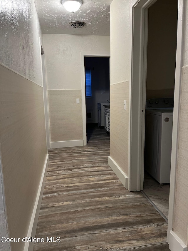 hallway with a textured ceiling, hardwood / wood-style floors, and washer / dryer