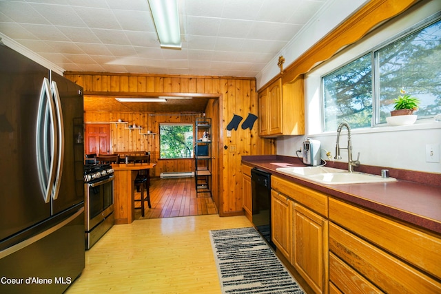 kitchen with light hardwood / wood-style floors, appliances with stainless steel finishes, sink, wood walls, and ornamental molding