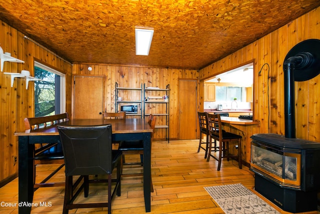 dining space featuring sink, light hardwood / wood-style flooring, wood walls, and a wood stove