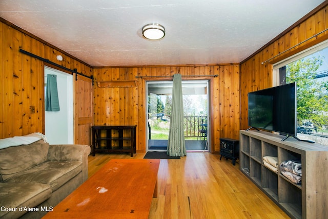 living room featuring a barn door, crown molding, hardwood / wood-style flooring, and wooden walls