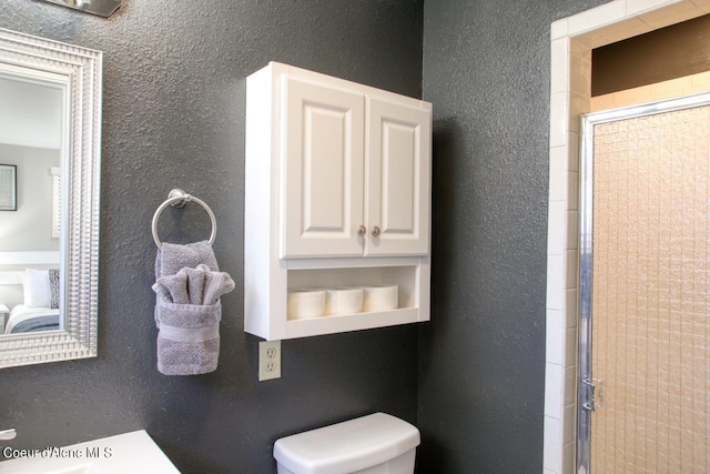 bathroom featuring a shower with door and toilet