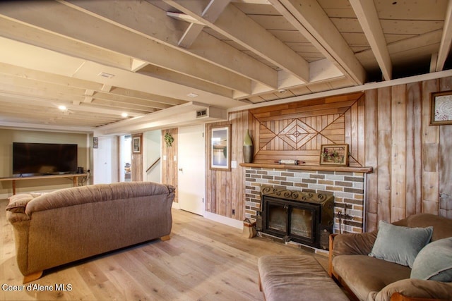 living room featuring beamed ceiling, light wood-type flooring, wood walls, and a fireplace