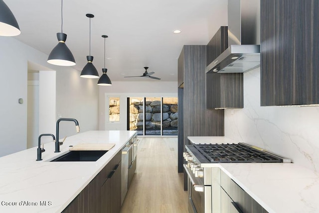 kitchen with wall chimney exhaust hood, sink, decorative light fixtures, appliances with stainless steel finishes, and light stone countertops