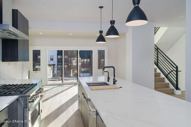 kitchen with sink, hanging light fixtures, light stone countertops, stainless steel gas range, and wall chimney exhaust hood