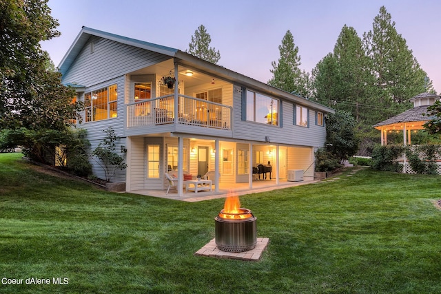 5718 E Sleepy Ln, Coeur Dalene, ID 83814 - back of house at dusk with a balcony, a fire pit, a patio, and a yard