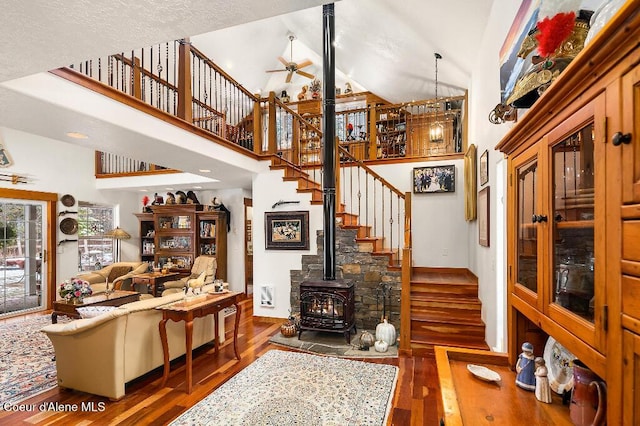 living room with ceiling fan, dark hardwood / wood-style floors, a wood stove, and a towering ceiling