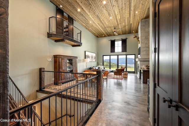 hallway with wooden ceiling, recessed lighting, concrete floors, a towering ceiling, and an upstairs landing