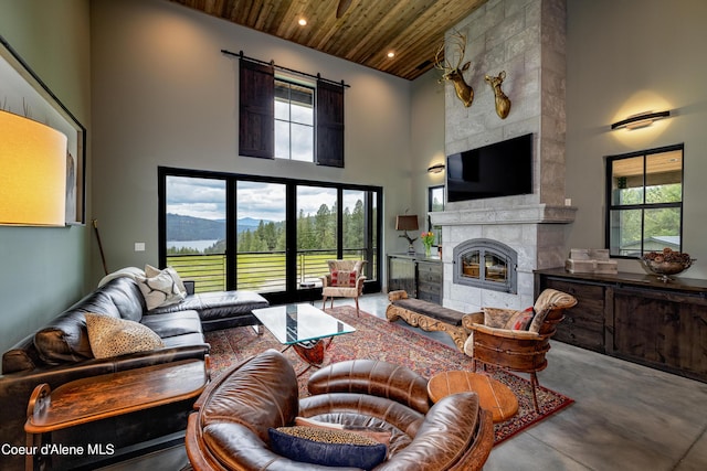 living room with a tile fireplace, wooden ceiling, a high ceiling, concrete floors, and a wealth of natural light