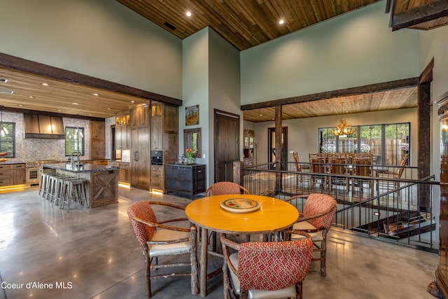 dining area featuring finished concrete floors, wooden ceiling, a chandelier, and a high ceiling