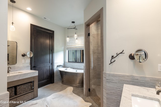 full bathroom featuring tile walls, a soaking tub, visible vents, and vanity