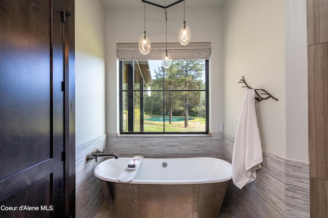 bathroom with a soaking tub, a wainscoted wall, and tile walls