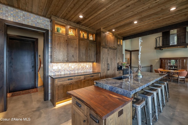 kitchen with a kitchen island with sink, glass insert cabinets, concrete flooring, and a sink