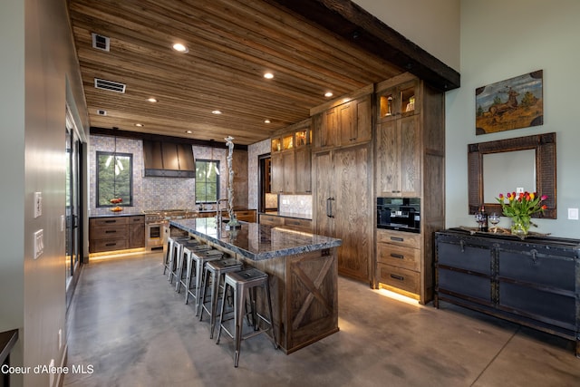 kitchen with concrete flooring, a spacious island, hanging light fixtures, wall chimney exhaust hood, and glass insert cabinets