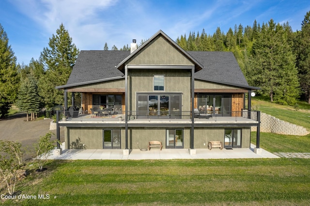 back of property with a patio, a chimney, stucco siding, a shingled roof, and a lawn